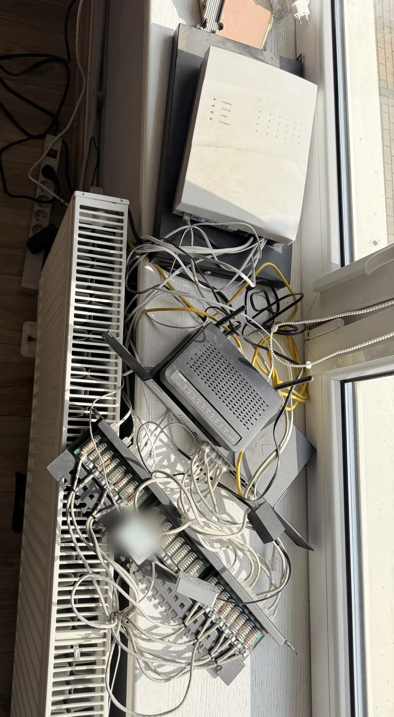 Router, przełącznik, centrala telefoniczna i splątane przewody ułożone na parapecie nad grzejnikiem